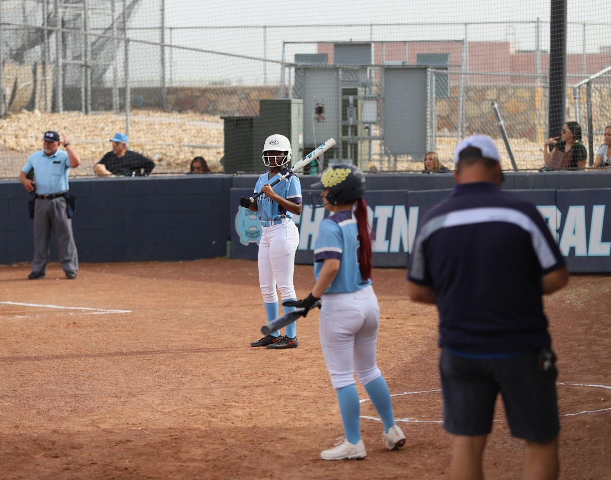 Player gets ready to bat, but looks on into the dugout listening to the cheering of her fellow teammates