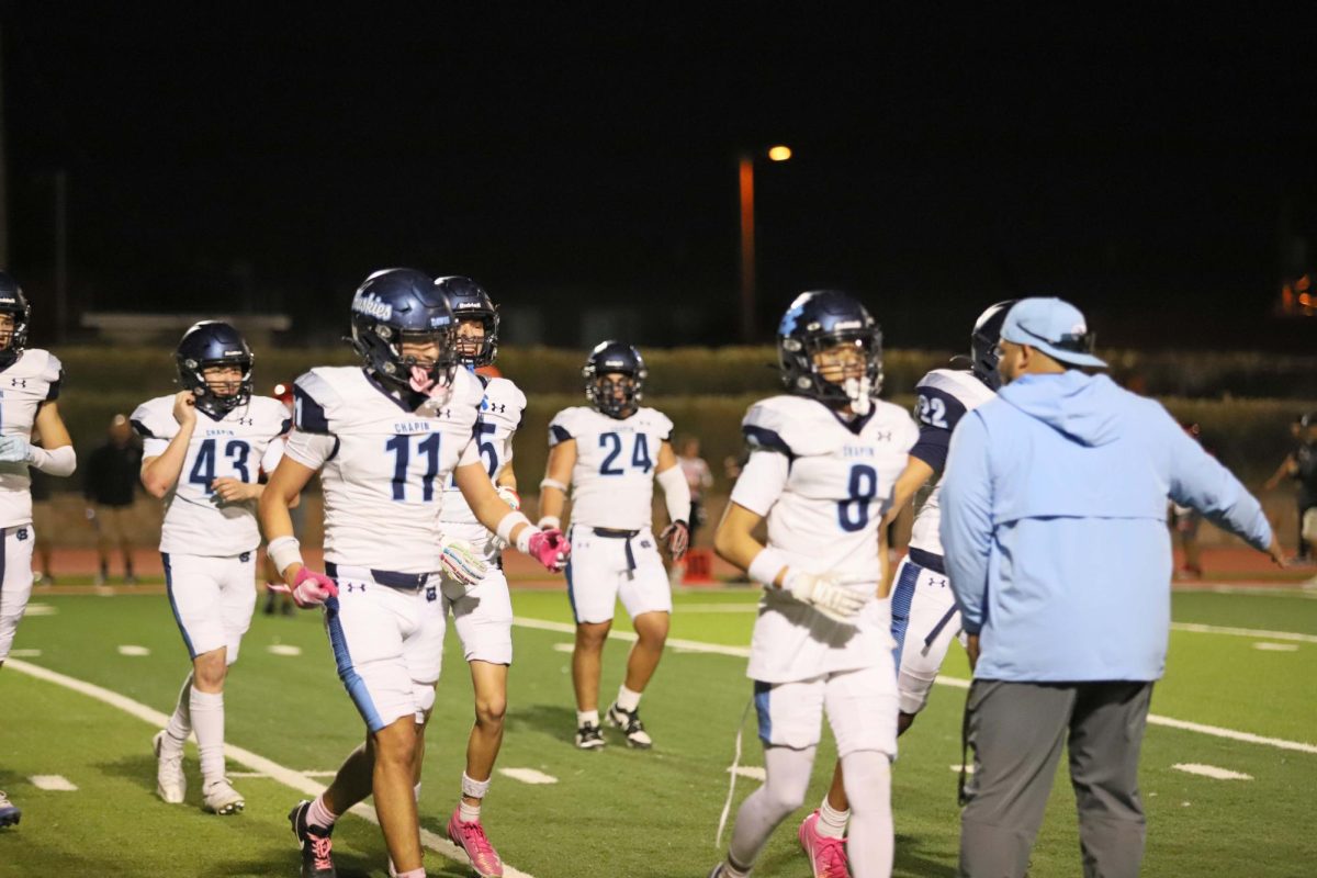Encouragement on the sidelines as Jv players run off the field after a play. The coach high fives each player, keeping the team's energy up between plays. 